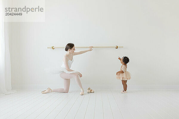 Adult Ballerina shows BIPOC baby ballet barre in white studio