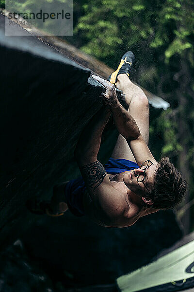 Shirtless climber with tattoo climbing a steep boulder