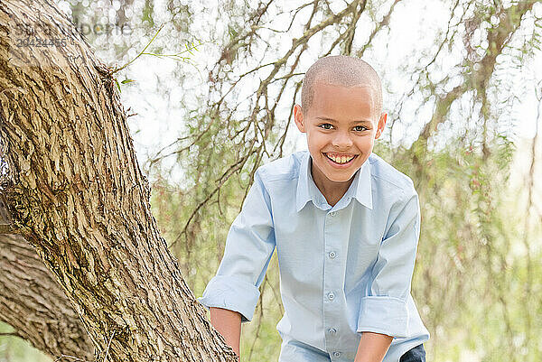 Smiling boy climbing tree with greenery around