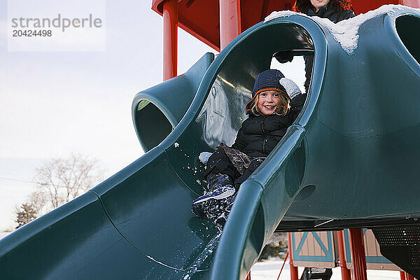 Smiling child sliding down a playground slide in winter