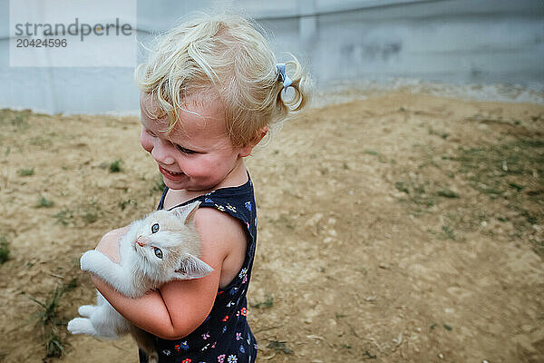 Smiling child tenderly holding a white kitten