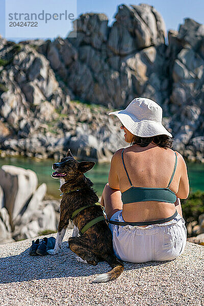 Back view of woman looking at dog laughing on a rocky landscape