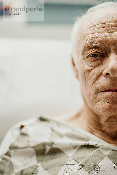 Portrait of tired looking elderly man in hospital wearing gown.