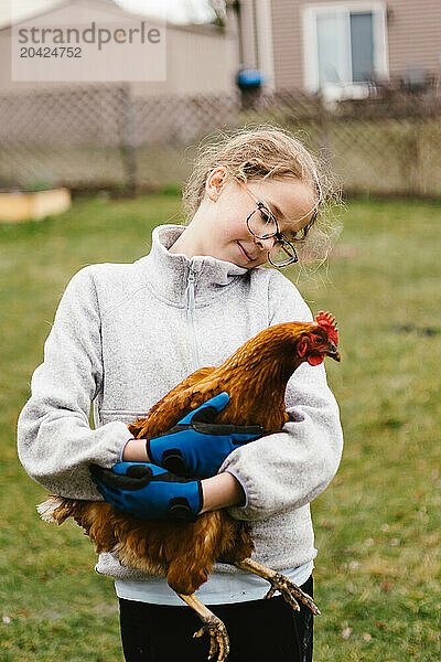 Girl looks at and holds mother hen chicken in green back yard