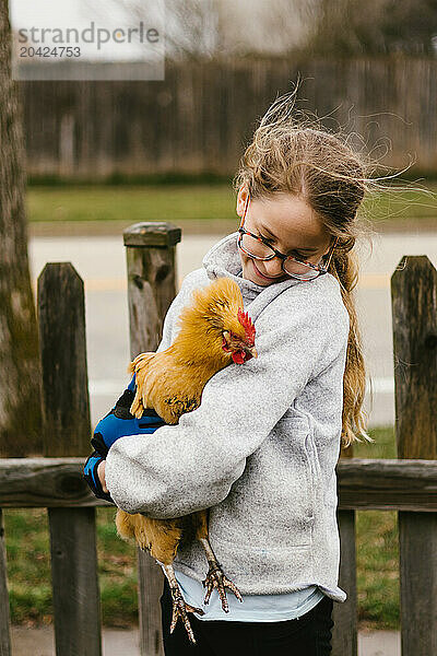 Girl with blond hair holds chicken and looks at it lovingly