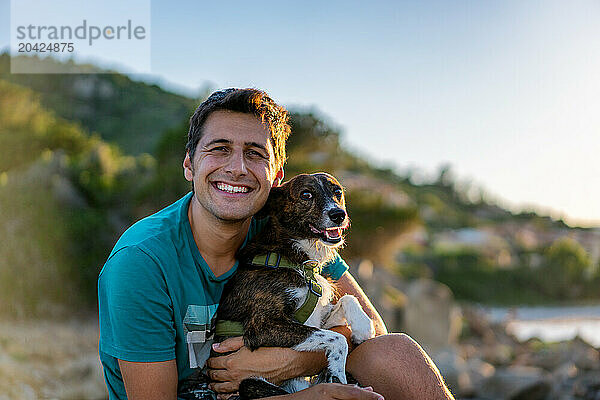 Man and dog smilling at the camera on a wild landscape and sunny day