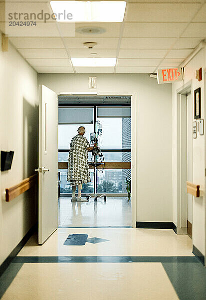 Elderly cancer patient wearing gown looks out window of hospital