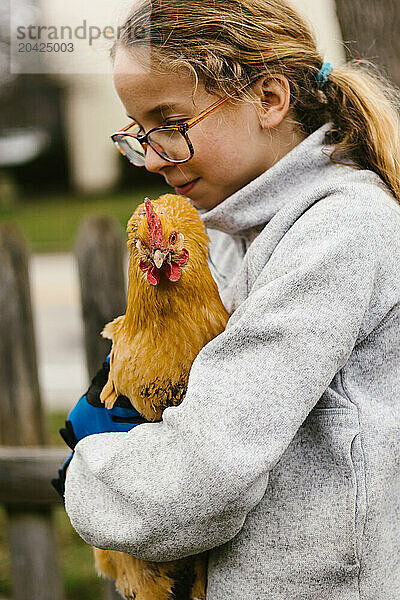 Girl holds pet golden chicken or hen in backyard of home