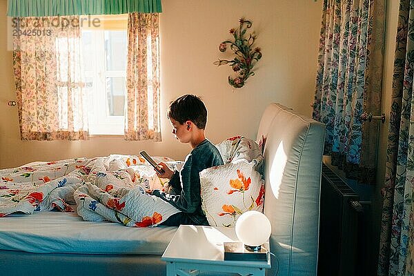 Teen boy playing on the phone at home in the sunlight