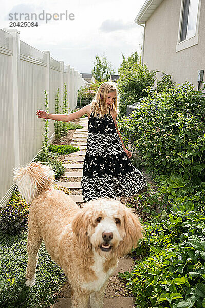 Pre-teen girl and fluffy dog walking together on a garden path.