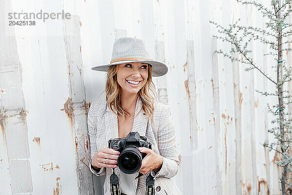 Woman with camera smiling by rustic wall