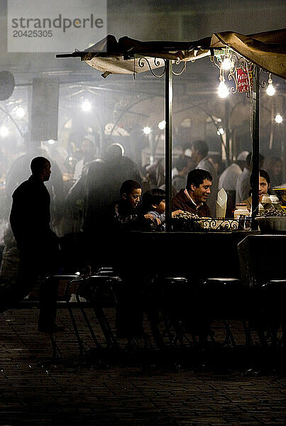 A family eats dinner at a stall at the evening market of the Djemaa el Fna in Marrakech  Morocco  in North Africa.