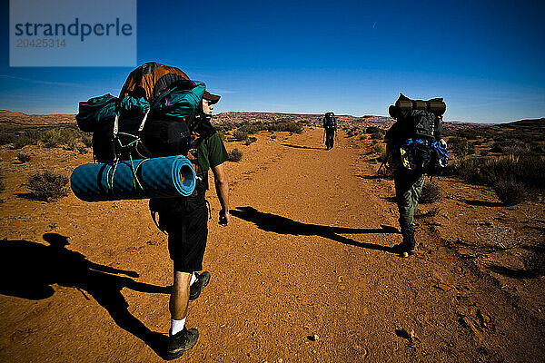 Three people hike along a dirt trail while backpacking in Grand Staircase-Escalante National Monument in Utah.