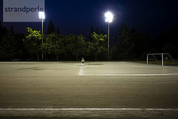 A lone soccer player stands in a soccer field at night in Seattle WA.