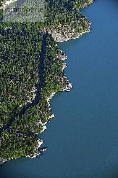 An aerial view of a strip of shoreline  forest  and railroad on the Howe Sound in Squamish Canada.