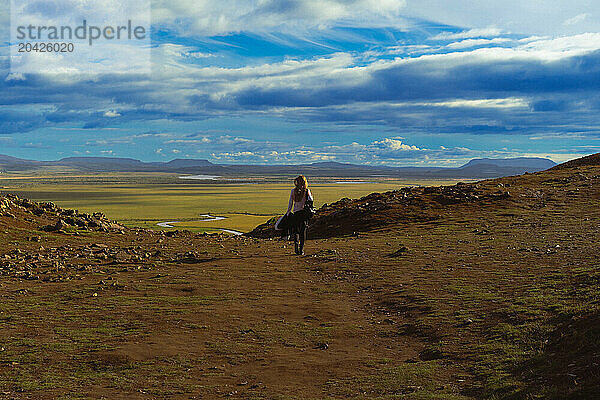 Woman hike on green hills over valley in mountains with clouds.