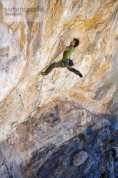 Professional rock climber lunging for a hand hold on a steep over hanging rock wall in South West Utah.