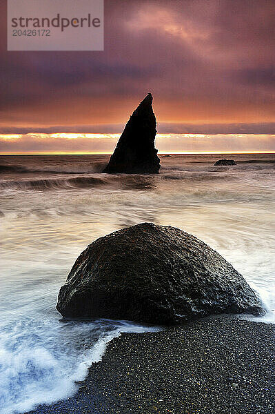 Waves crashing over a beach boulder on Ruby Beach in Olympic National Park at sunset.