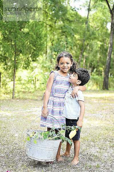 Happy siblings holding a basket of harvested vegetables  smiling outdo