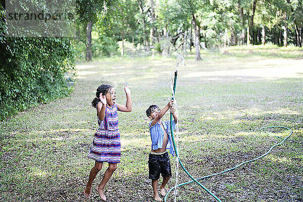 Two children playing with a garden hose in a backyard  laughing