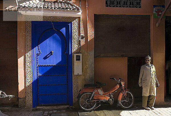 A man stands in front of a brightly colored door on Rue de Bab Taghzout  in the old fortified city section of Marrakech  Morocco.