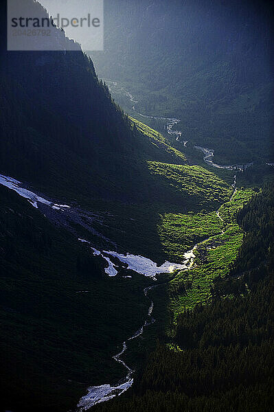 An aerial view of a shaft of light and long cascading river cutting down the center of a canyon and highlighting the forest in Squamish  British Columbia  Canada.