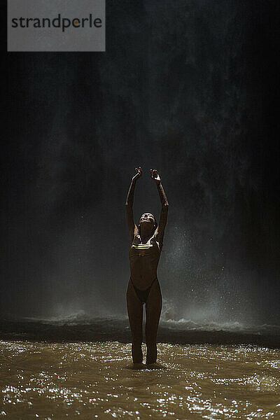 Woman enjoying under waterfall flowing over rock formation