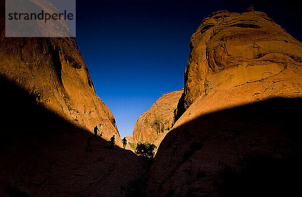 Three people hike through Coyote Wash as the sun sets in Grand Staircase-Escalante National Monument in Utah.