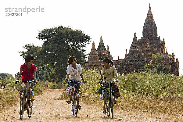 Local girls bicycle among the historic pagodas of Bagan