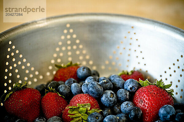 A strainer full of blueberries and strawberries.