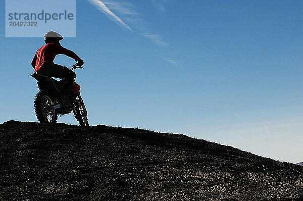 A young man takes a break from riding his dirt bike during a motocross trip to the surreal dunes of the Painted Desert near Cameron  AZ.