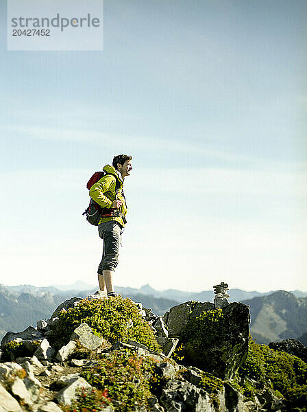 A male hiker on a mountain top looks off into the distance.