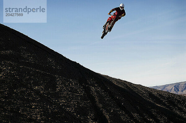 A young man jumps his dirt bike high in the air while motocross riding the surreal dunes near Cameron  AZ.