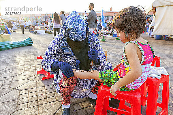 Small Girl Getting Henna Tattoo On Her Leg At Main Square Of Marrakech  Morocco