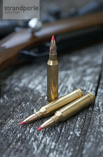 Detail  selective focus shot of 7 mm rifle ammunition resting on a wooden table next to a gun.