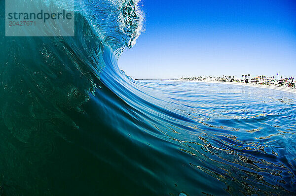 Water angle of an ice blue wave breaking offshore of a palm lined beach with a pier in the background.