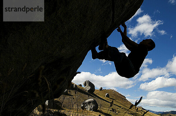 A young male rock climber is silhouetted against the sky in Castle Hill  New Zealand.