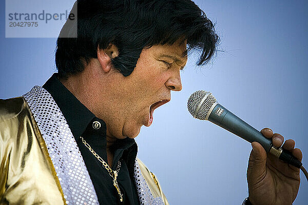 Elvis impersonator holding a microphone on stage performing in front of a crowd.