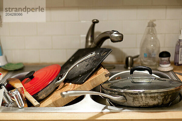 Piles of dirty pots and pans in a kitchen sink in a home.