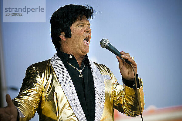 Elvis impersonator holding a microphone on stage performing in front of a crowd.