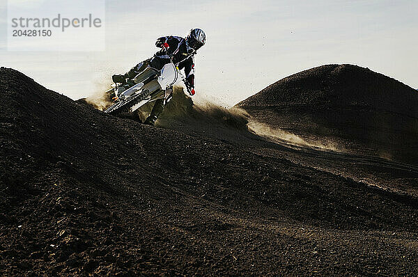 Dust and dirt fly as a young man banks his dirt bike into a hard turn while motocross riding on the surreal dunes near Cameron  AZ.