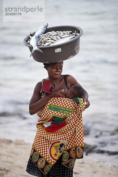 Mother breastfeeding baby while carrying bowl of fish on top of head  Inhambane  Mozambique