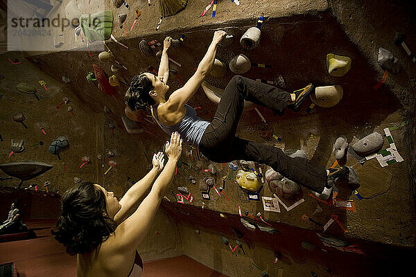 Female rock climbers boulder in a rock climbing gym.