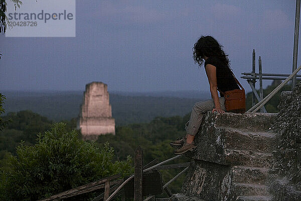 A woman overlooks Mayan ruins in the jungle.