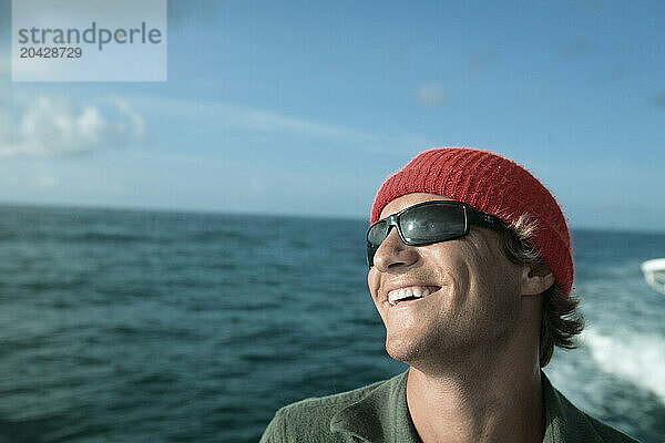 A man looks off the bow of a boat and laughs under a cloudy sky on a fishing trip.