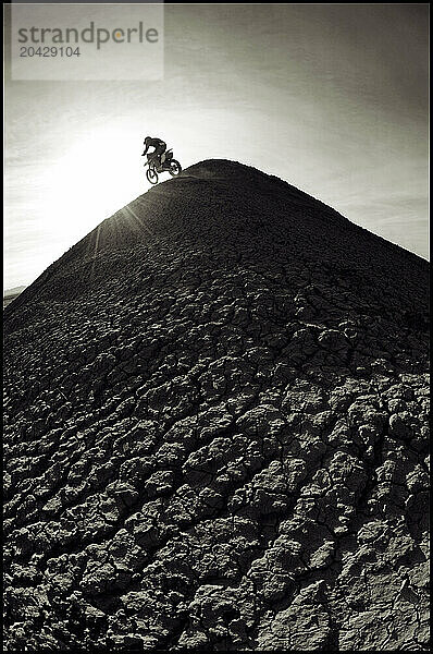 A young man rides his dirt bike up and over a steep hill while motocross riding the surreal dunes near Cameron  AZ.