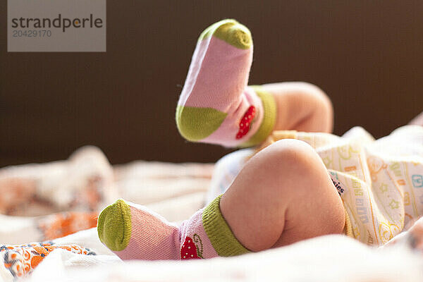 Close up of a newborn baby's legs kicking on a couch in a home.