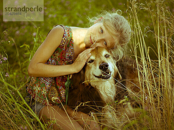 a girl sits in the grass and hugs her dog