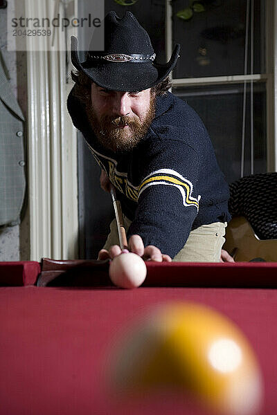 Young man with beard playing pool.