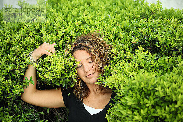 A young woman enjoys the feel of a lush green plant on her face